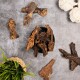 Eine schwarze Schüssel, gefüllt mit verschiedenen Stückchen von Trockenfleisch-Leckerlis für Haustiere, umgeben von verstreuten Stücken und einer kleinen grünen Pflanze.