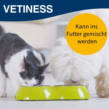 Eine schwarz-weiße Katze und ein flauschiger weißer Hund fressen aus einer grünen Schüssel, mit "VETINESS" und einem gelben Kreis, der sagt: "Kann ins Futter gemischt werden."