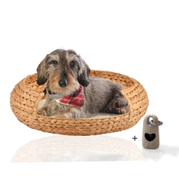 Ein gemütliches gewebtes Hundebett mit einem grauen Hund, der ein rotes Karobandana trägt und darin ruht, begleitet von einem kleinen herzförmigen Etikett.