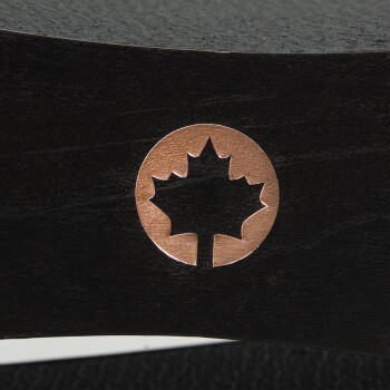 Nahaufnahme einer schwarzen Holzoberfläche mit einem kupfernen Ahornblatt-Emblem, das in runder Form ausgeschnitten ist.