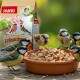 Kleine Vögel, die Erdnüsse aus einer braunen Schale neben einer PANTO Premium Erdnussbruch Vogelfuttermischung fressen.