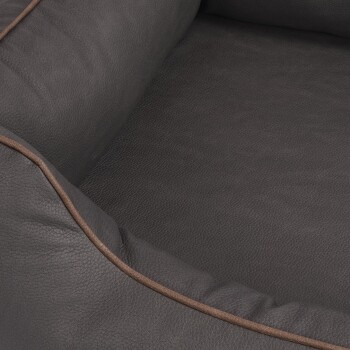 Eine Nahaufnahme eines dunkelgrauen Haustierbettes mit einer weichen, lederähnlichen Textur und einem kontrastierenden braunen Rand entlang der Kante.