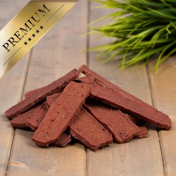 Premium-Hundeleckerlis, die auf einer Holzoberfläche gestapelt sind, mit einem goldenen 'PREMIUM'-Abzeichen in der Ecke und grünem Gras im Hintergrund.