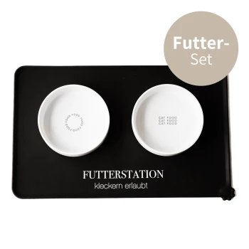 Weiße Katzenfutterschalen auf einem schwarzen Tablett, mit der Aufschrift "KATZENFUTTER", mit dem Text "FUTTERSTATION kleckern erlaubt" darüber.
