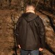 Person trägt eine dunkelgrüne Outdoor-Jacke mit großen Taschen, steht in einem sonnenbeschienenen Wald mit kahlen Bäumen.
