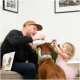 Mann und Kind füttern einen braunen Hund mit blauem Halsband; Leckerlitasche auf dem Sofa mit der Aufschrift 'DENTAL'.