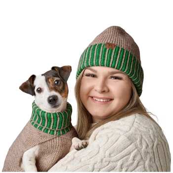 Eine Frau hält einen kleinen Hund, der einen grün-braun gestreiften Pullover und ein passendes Halsband trägt, beide sehen gemütlich und stilvoll aus.
