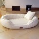 Cremefarbenes ovales Haustierbett mit passendem Kissen auf gefliestem Boden, mit kleinem braunem Etikett vorne.