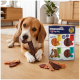 Beagle kaut an einem Trockenfleisch-Snack auf dem Boden neben einer 'PREMIERE. I ♥ my dog' XXL 'Meaties'-Packung und verstreuten Leckerlis.