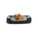 Ein kleiner brauner Hund liegt bequem auf einem plüschigen, grauen und schwarzen Haustierbett und schaut in die Kamera.