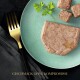 Ein grüner Teller mit Haustierfutter-Pâté, kleinen Würfeln und Petersilie; eine goldene Gabel daneben. Text: "GESCHMACK OHNE KOMPROMISSE."