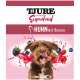 Ein verspielter brauner Hund mit herausgestreckter Zunge auf einer Haustierfutterverpackung mit der Aufschrift "TJURE das Original Superfood" mit "HUHN mit Beeren" und Beerenspritzern.
