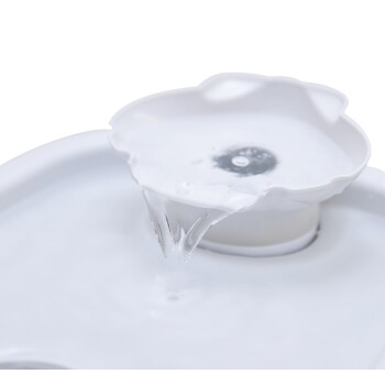 Ein weißer Haustier-Wasserbrunnen mit einer blumenförmigen Oberseite, mit einem sanften Wasserstrahl, der aus der Mitte in die Schüssel darunter fließt.