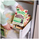 Eine Person hält ein Paket "Lamm, Kürbis & Brokkoli" Hundefutter von Nutriment, mit einem schwarzen Hund auf dem Etikett, in einer Gefrierlade.