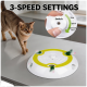 Getigerte Katze neben weißem, kreisförmigem Spielzeug mit grünem Ring und rotierenden Federn auf einer Arbeitsfläche; Text '3-SPEED SETTINGS'