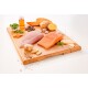 Ein Holzschneidebrett hält frische Zutaten für Haustierfutter: roher Lachs, Hähnchen, Süßkartoffel, Erbsen, Karotten, Ingwer, Apfelscheiben und Öl.