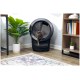 Eine graue Katze kommt aus einer modernen schwarzen Katzentoilette, mit einer grünen Topfpflanze in der Nähe und einem Bücherregal im Hintergrund.