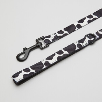 Eine stilvolle Hundeleine mit einem schwarz-weißen Kuhflecken-Design, mit einem stabilen schwarzen Clip zur Befestigung.