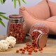 Zwei Glasbehälter mit roten Haustierleckereien, einer auf einem Holztisch verschüttet, mit einem weißen Seilspielzeug und einem rosa Haustierbett im Hintergrund.