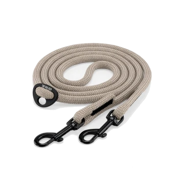 Aufgerollte beige, geflochtene doppelseitige Hundeleine mit zwei schwarzen Metallwirbelkarabinern und einem schwarzen Etikett mit der Aufschrift 'THE DOG IDEA'.