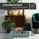Ein kleiner Hund ruht sich in einem gemütlichen blauen Haustierbett aus, umgeben von stilvoller Wohnkultur, mit dem Text "ZUM EINKUSCHELN schafft ein gemütliches Ambiente" darüber.