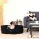 Ein gemütliches schwarzes Hundebett mit einem kleinen Hund, der darin ruht, platziert in einem stilvollen Wohnzimmer mit einem grauen Sofa, einem Couchtisch und einer Lampe.