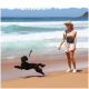 Eine Frau in einem beigen Outfit und Hut steht am Strand und beobachtet einen schwarzen Hund, der fröhlich mit einem Stock im Mund springt, mit Wellen im Hintergrund.