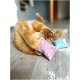 Un chat orange joueur roule sur le sol, tenant des coussins colorés à pois dans ses pattes, avec ses pattes en l'air.