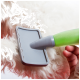 Eine Person verwendet eine grau-grüne Haustierpflegebürste auf dem Fell eines flauschigen weißen Hundes, um lose Haare zu entfernen.