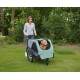 Frau schiebt grünen Haustier-Kinderwagen in einem Park mit einem Golden Retriever darin; kleines weißes Logo auf dem Anhänger