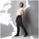 Eine Frau steht im Profil, trägt ein graues T-Shirt und schwarze Cargo-Hosen und zeigt einen lässigen Outdoor-Stil vor einem grauen Hintergrund.