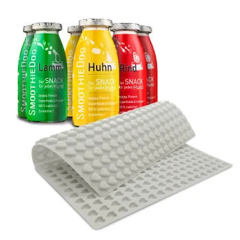 Vier bunte Smoothie-Flaschen für Hunde mit den Aufschriften "Lamm", "Huhn" und "Rind", neben einer rosa Silikonmatte mit Herzformen.