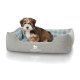 Ein kleiner, flauschiger Hund sitzt in einem gemütlichen grauen Haustierbett mit kariertem Innenraum, mit dem Markennamen "KNUFFELWUFF" auf der Vorderseite.