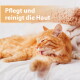 Rote Katze putzt sich auf dem Bett neben gefalteten Handtüchern; deutscher Text: 'Pflegt und reinigt die Haut'.