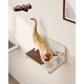 Eine rote Katze frisst aus einer doppelten Futterschüssel an einer wandmontierten Station, mit einer braunen Matte darunter und dem Logo "clickat by feandrea" in der Ecke.