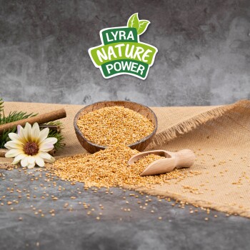 Eine Holzschüssel mit gelben Samen steht auf Jute, mit verschütteten Samen und einem Schaufel in der Nähe. Eine weiße Blume und "LYRA NATURE POWER" sind darüber.