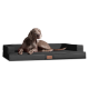 Ein grauer Weimaraner-Hund, der auf einem schwarzen rechteckigen Haustierbett mit erhöhten Rändern entspannt, mit einem kleinen Lederetikett mit dem Markenlogo.