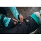 Eine Person befestigt einen silbernen Clip an einer schwarzen Hundejacke mit einem türkisfarbenen Kragen, die ein Ruffwear-Logo trägt.