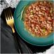 Une assiette teal contenant une portion de nourriture pour animaux avec de petits morceaux de viande dans une sauce, garnie d'herbes vertes, à côté d'une fourchette dorée.