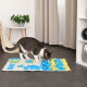 Gestromte und weiße Katze schnüffelt an einer blau-gelben Stoff-Snuffle-Matte auf grauem Boden in einem Wohnzimmer.
