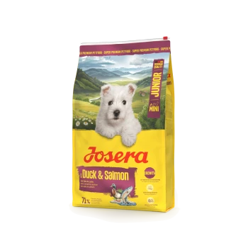 Josera Junior Mini Ente & Lachs Hundefutterbeutel mit weißem Welpen und malerischem Bergpanorama im Hintergrund.