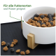 Weiße Futterschüssel für Haustiere mit braunem und schwarzem Futter, die auf einer schwarzen Matte ruht, beschriftet mit 'Für alle Futterarten und Wasser geeignet.'