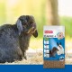 Un lapin noir est assis sur de la paille, regardant en haut, à côté d'un sac de nourriture pour animaux Beaphar Care+ avec un lapin blanc et un lapin gris sur l'emballage.