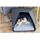 Ein kleiner braun-weißer Hund, der in einem modernen grauen Haustierbett mit dreieckiger Form auf einem Holzboden entspannt.