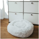 Flauschiges weißes Haustierbett auf einem Holzboden neben einem modernen weißen Aufbewahrungseinheit mit metallischen Knöpfen.