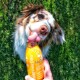 Ein glücklicher Hund leckt eine Flasche "Smoothie Dog" Hühnergeschmack Snack, gehalten von einer Person, mit grünem Gras im Hintergrund.