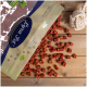 Eine Tüte Katzenleckereien mit dem Etikett "Feline Fit" lässt kleine, rote, würfelförmige Leckereien auf eine Holzoberfläche fallen, neben einem weißen Seilspielzeug.