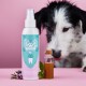Eine türkisfarbene und rosa "DENTALSPRAY"-Flasche, ein Glasgefäß, ein Minzzweig und ein neugieriger schwarz-weißer Hund im Hintergrund.
