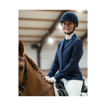Ein Reiter in einer marineblauen Reitjacke und einem Helm sitzt auf einem braunen Pferd und zeigt eine konzentrierte Haltung in einer Indoor-Arena.