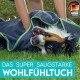 Eine Person wickelt einen glücklichen Hund in ein dunkelgraues Handtuch mit grünem Rand auf Gras. Text lautet "DAS SUPER SAUGSTARKE WOHLFÜHLTUCH."